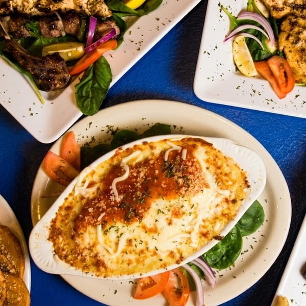 Overhead view of a blue table laden with various Greek dishes, including gyros, baked pasta, and grilled meats.