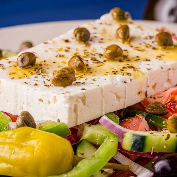 Close-up of a Greek salad with a large block of feta cheese, capers, and fresh vegetables.