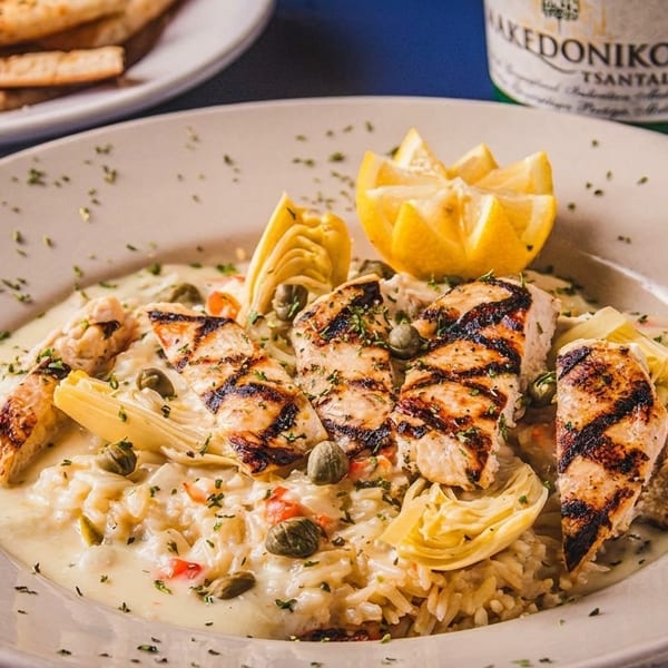 Grilled chicken and rice pilaf with artichokes, capers, and lemon, served with pita bread and wine.