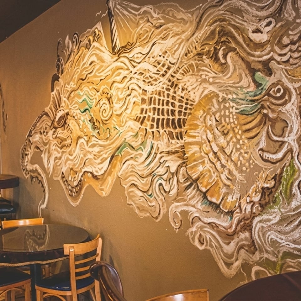 Restaurant interior with a large, colorful mural on a brown wall, and several tables with chairs.